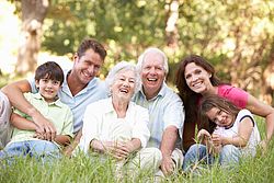 Drei Generationen einer Familie sitzen im Gras und lachen in die Kamera.